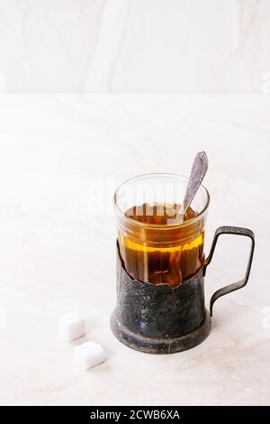 Retro cup of hot tea in vintage glass-holder with tea spoon and sugar cubes over white marble backgtound. Stock Photo