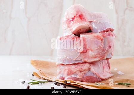 Stack of raw osso buco meat on crumpled paper with salt, pepper and rosemary over white marble as background Stock Photo