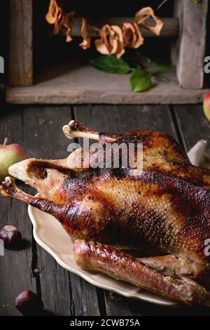 Roast stuffed goose on ceramic plate with ripe apples over wooden kitchen table. Dark rustic style. Stock Photo