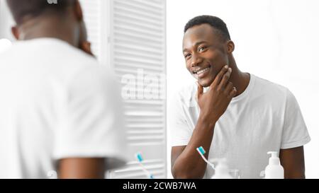 Well-Shaved African Man Touching Smooth Face After Shaving In Bathroom Stock Photo