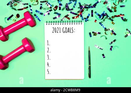 Goals list for New Year Holiday. Christmas sport set with dumbbells, notebook with pen and colorful confetti on on pastel mint green blue background. Flat lay, top view, copy space. Stock Photo