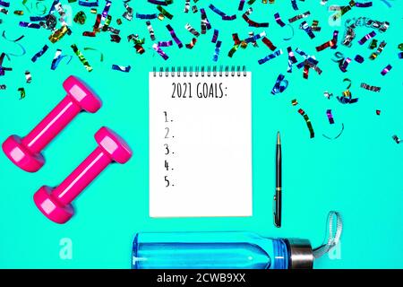 Goals list for New Year Holiday. Christmas sport set with dumbbells, notebook with pen, bottle of waterwater and colorful confetti on mint green blue color background. Flat lay, top view, copy space. Stock Photo