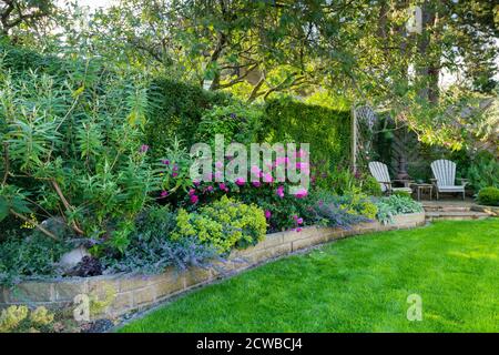 Landscaped sunny private garden (contemporary design, colourful summer flowers, border plants, patio furniture seating, lawn) - Yorkshire, England, UK Stock Photo