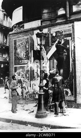 Billboard with men putting up propaganda posters, Paris, World War II, 1939-1945. The photographer is unknown. Stock Photo