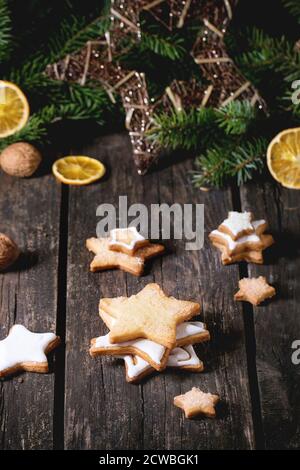 Christmas glazed star shapes cookies with Christmas tree and dry sliced orange over old wooden table. Rustic style. View from outside Stock Photo