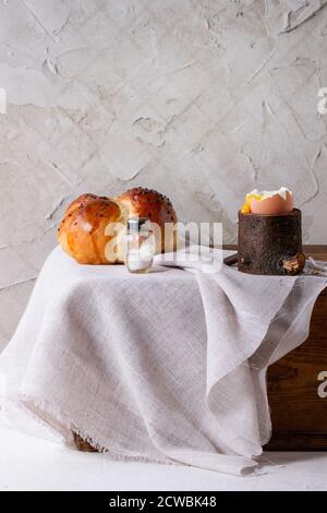 Breakfast with started eating soft-boiled egg with pouring yolk in wooden eggcup and bread served with salt on wooden chest with white cloth over whit Stock Photo