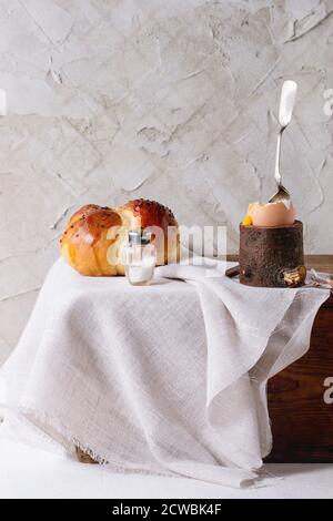 Breakfast with started eating soft-boiled egg with pouring yolk in wooden eggcup and home made bread served with salt and silver spoon on wooden chest Stock Photo