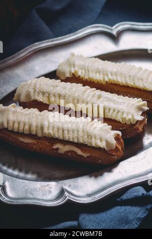 Home made Eclairs with white butter cream in vintage metal plate. Dark rustic style. Day light. Outside view Stock Photo