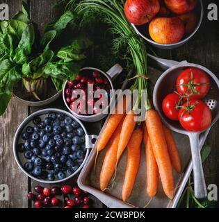 Assortment of fresh fruits, vegetables and berries. Bunch of carrots, spinach, tomatoes and red apples, blueberries and cranberries in vintage aluminu Stock Photo