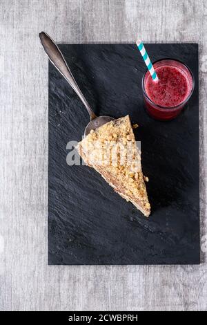 Piece of Homemade Honey Cake with chocolate cream, served with glass of red juice with striped cocktail tube on black slate board over white wooden ta Stock Photo