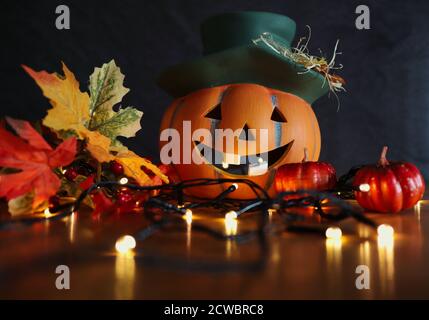 Ceramic Halloween Orange Pumpkin with Smile with Artificial Autumn Leaves and Blinking Lights. Autumn and Halloween Vibes. Stock Photo