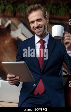 smiling young businessman drinking coffee and holding tab in a coffeeshop Stock Photo