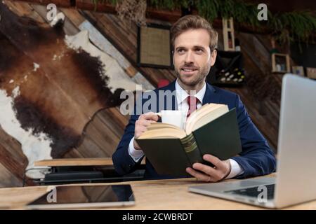 happy businessman drinking a coffee and reading a book, looking to side in a coffeeshop Stock Photo