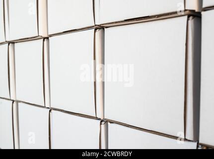 Side view of white paper boxes in rows, minimalistic design objects. Wall with cardboard square shaped empty packages in delivery room, closeup view, Stock Photo