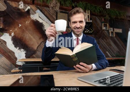 happy businessman drinking coffee and reading a book, sitting in a coffeeshop Stock Photo