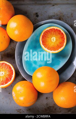 Sliced and whole Sicilian Blood orange fruit on bright turquoise and gray ceramic plates over rusty metal background. Flat lay Stock Photo