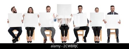 Team of 7 businessmen holding empty billboards while one is hiding her face and other one is screaming sitting on chairs on white studio background Stock Photo