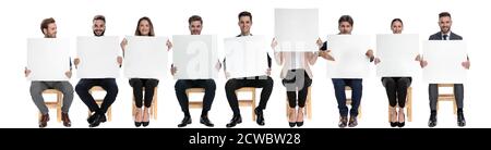 Team of 9 businessmen holding empty billboards while one is hiding her face, sitting on chairs on white studio background Stock Photo
