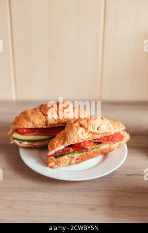 Fresh french croissant with salmon and cucumber on a plate on a wooden table. Vertical photo orientation Stock Photo