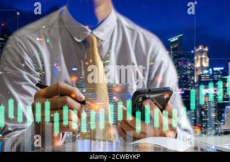 Double exposure financial graph and businessman using smartphone and pen with cityscape on blurred building background. Stock Photo