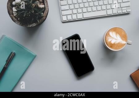 Office desk with keyboard, computer, smartphone, notebook, coffee and cactus on gray vintage tone background.Top view with copy space. Business and fi Stock Photo