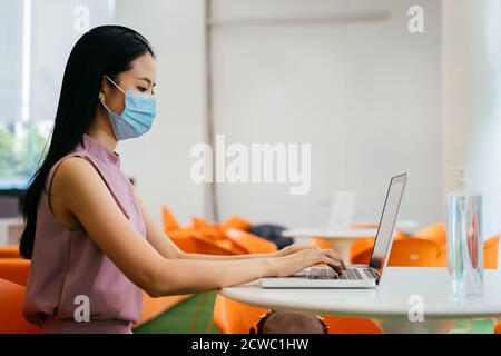 Asian businesswoman wearing protective Covid face covering working in modern office, using computer, concentration, protection, health Stock Photo