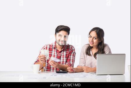 Focused Indian young couple accounting, calculating bills, discussing planning budget together using online banking services and calculator, checking Stock Photo