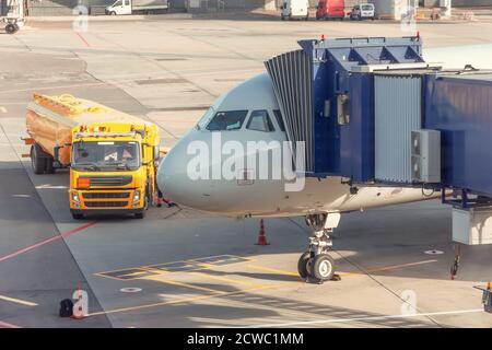 Aircraft in the parking lot is attached to the boarding bridge for boarding passengers from terminal building, truck with fuel tank, refueling Stock Photo