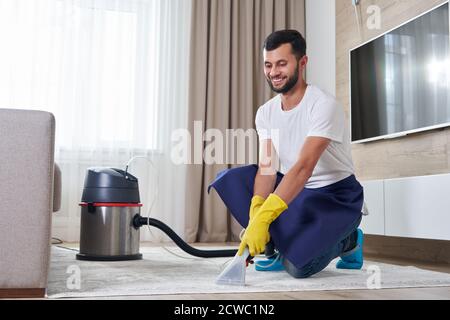 Man Cleaning Carpet In The Living Room Using Vacuum Cleaner At Home. Cleaning service concept Stock Photo