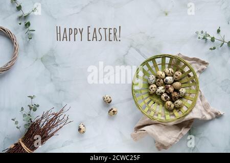 Quail Easter eggs, natural Spring decorations and eucalyptus twigs. Flat lay on marble table, text Happy Easter. Stock Photo