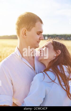 Smiling happy couple. Handsome Caucasian man wearing white shirt gentle hugs a smiling young woman with blond hair in dress. Stock Photo