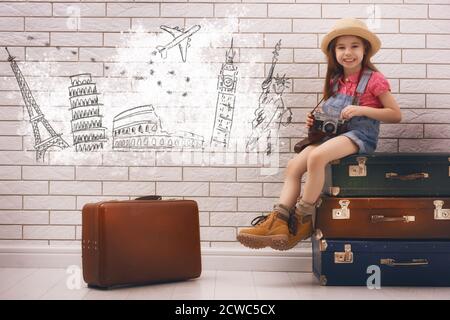 happy child girl against a white brick wall. girl having suitcases and dreaming of traveling. Stock Photo