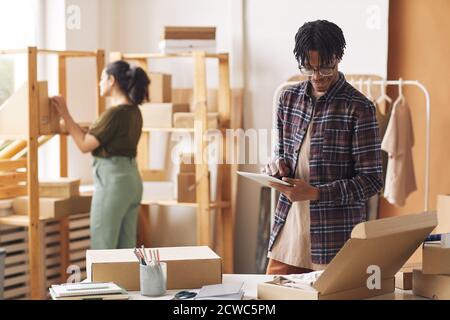 Man checking parcels using digital tablet he packing boxes in warehouse with woman working in the background Stock Photo
