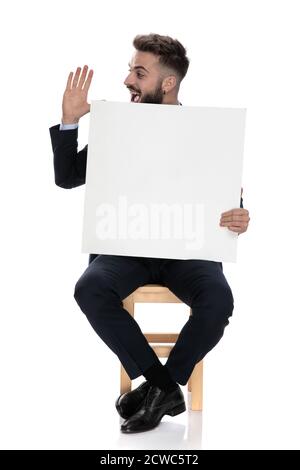 young businessman smiling and holding hands up, holding empty board and saluting, sitting isolated on white background Stock Photo