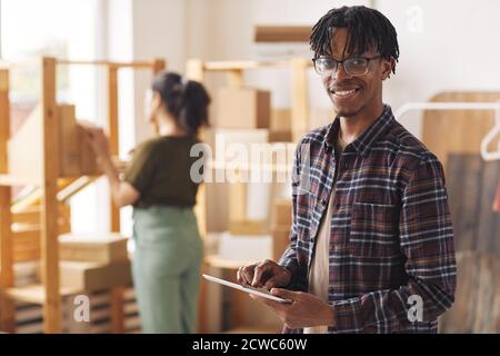 Portrait of young African man smiling at camera while working with digital tablet in warehouse Stock Photo
