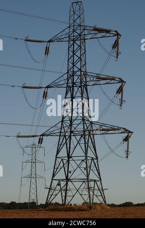 Two transmission towers, electricity pylons, against a blue sky in a field Stock Photo