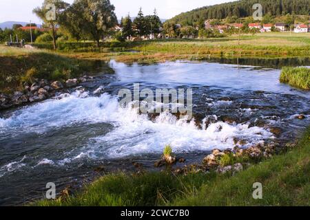 Beautiful Gacka river flowing between trees and fields, summer view, Lika region of Croatia Stock Photo