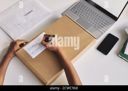 Close-up of man sitting at the table in front of the laptop and filling the form on the parcel he writing his address Stock Photo