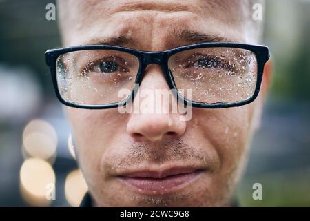 Portrait of young man with eyeglasses in rain. Selective focus on raindrops. Stock Photo