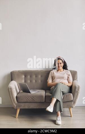 Portrait of young happy woman smiling at camera while sitting on sofa with laptop computer Stock Photo