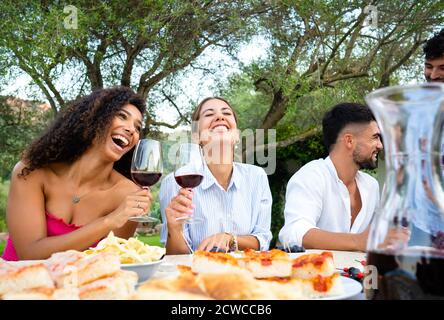 Mixed group of young happy friends celebrating outdoor with snacks and alcoholic drinks - Selective focus on the two cute smiling young hispanic and c Stock Photo