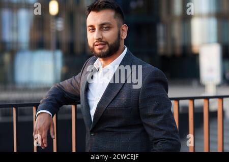 Portrait of young confident businessman in elegant black suit looking at camera while standing at balcony Stock Photo