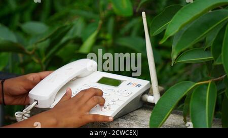 Closeup of male hand holding telephone receiver while dialing a telephone number to make a call using a white landline phone. Stock Photo