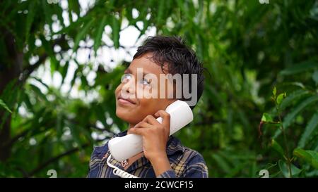 Cute Indian little boy holding the white phone, classic white telephone receiver in hand. Stock Photo