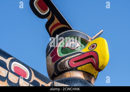 Colourful wooden carved Canadian totem pole showing eagle's head against blue sky Stock Photo