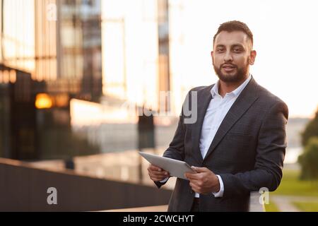 Portrait of young businesswoman in formal suit looking at camera while using digital tablet in the city Stock Photo