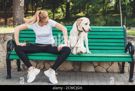 Caucasian lady and her labrador posing in park on a bench having a pause from walk Stock Photo