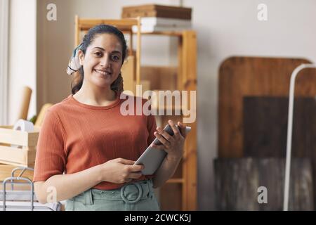 Portrait of young woman smiling at camera while using digital tablet during her work in warehouse Stock Photo