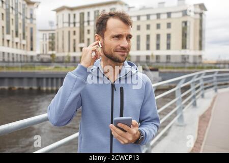 Young man wearing wireless headphones using his mobile phone to listen to music during his walk in the city Stock Photo