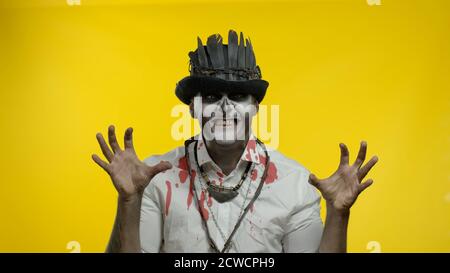 Sinister man with horrible Halloween skeleton makeup in costume with top-hat making faces, looking at camera trying to scare. Horror theme. Day of The Dead. Yellow background. Copy space Stock Photo
